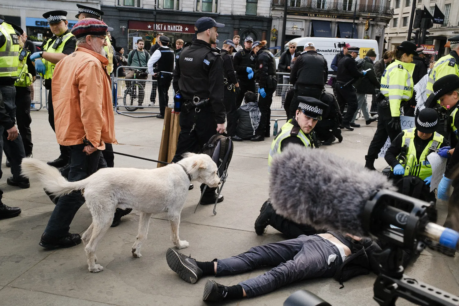 A dog beside a person lying on the pavement among police and onlookers