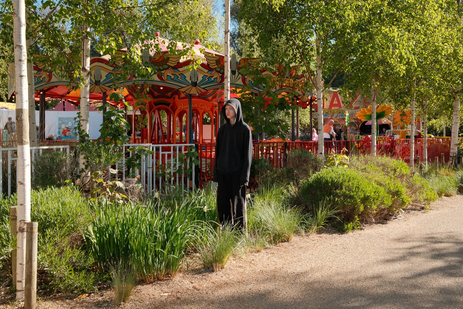 A black-cloaked figure standing beside a fairground carousel